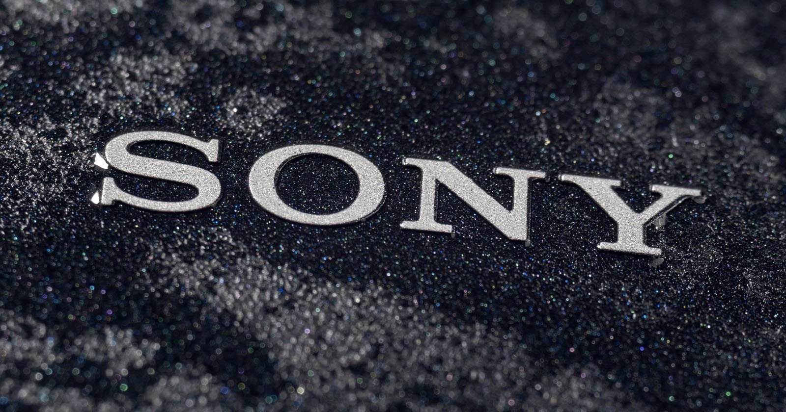 The image shows the Sony logo in silver letters placed on a textured, dark, glittery surface. The letters stand out against the sparkling, black background.